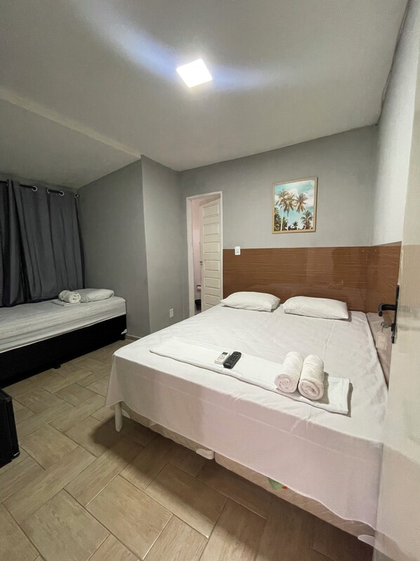A hotel room with two single beds, a large bed, a painting on the wall, and a ceiling light. - Pousada Encanto dos Mares (Natal)