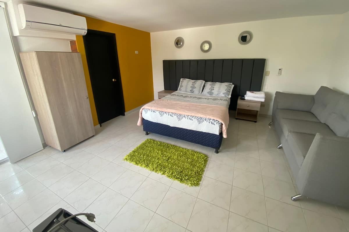 A bedroom with a bed, a grey sofa, a small table, and a green rug.