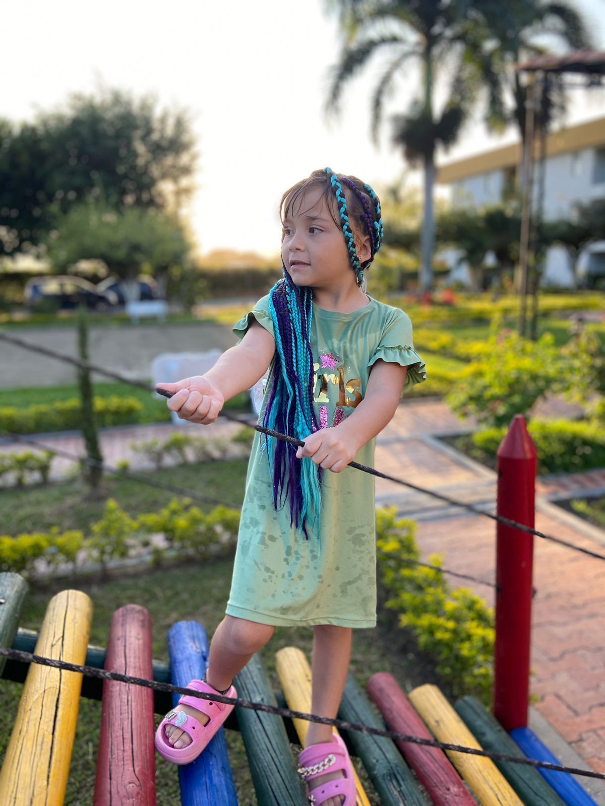 Criança brincando com um graveto em uma ponte suspensa num parque.
