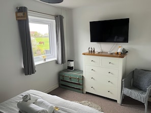 Une chambre à coucher avec un lit, une commode, un téléviseur, une valise et une fenêtre avec des rideaux.