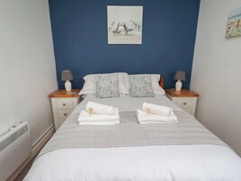 Una cama bien hecha con dos almohadas, una mesita de noche con una lámpara y una pared con un cuadro enmarcado.