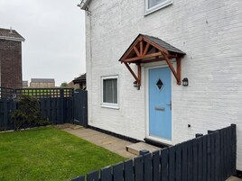 Un edificio blanco con una puerta azul, una ventana pequeña y un porche de madera.