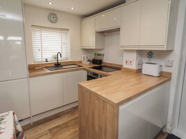 Cocina compacta con armarios blancos, encimera de madera, pileta, tostadora y un reloj en la pared.