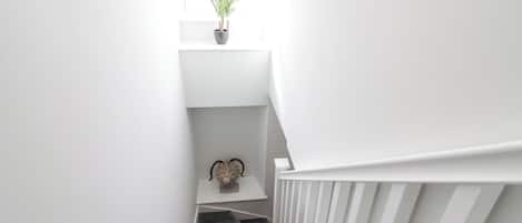 Una escalera estrecha con barandilla blanca, una planta en maceta en la parte superior y un objeto decorativo en el rellano.