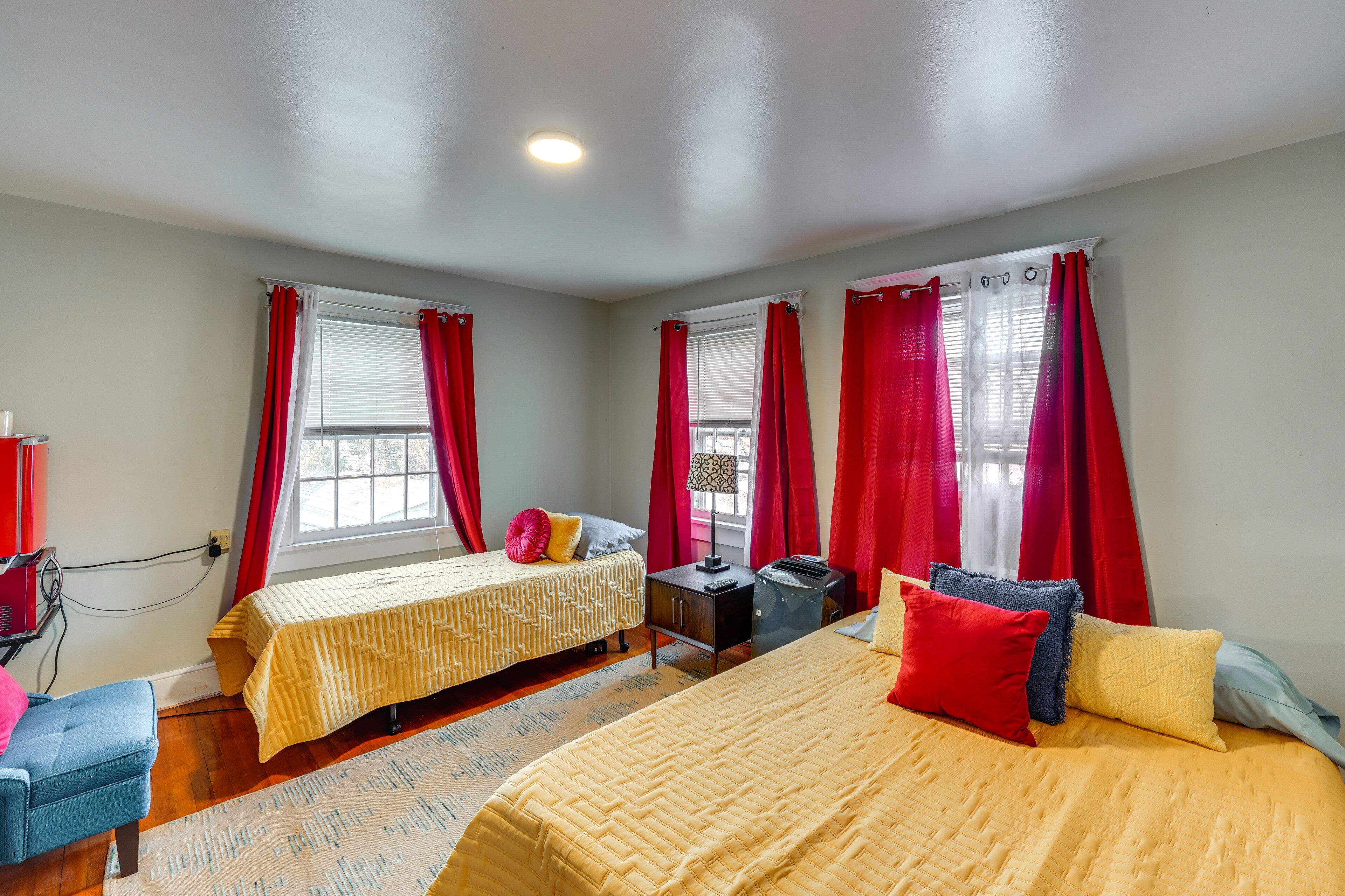A hotel room with two beds, red curtains, a desk, and a chair.
