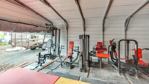 Zona de gimnasio techada con equipo de ejercicio, un camión y suelo de grava.