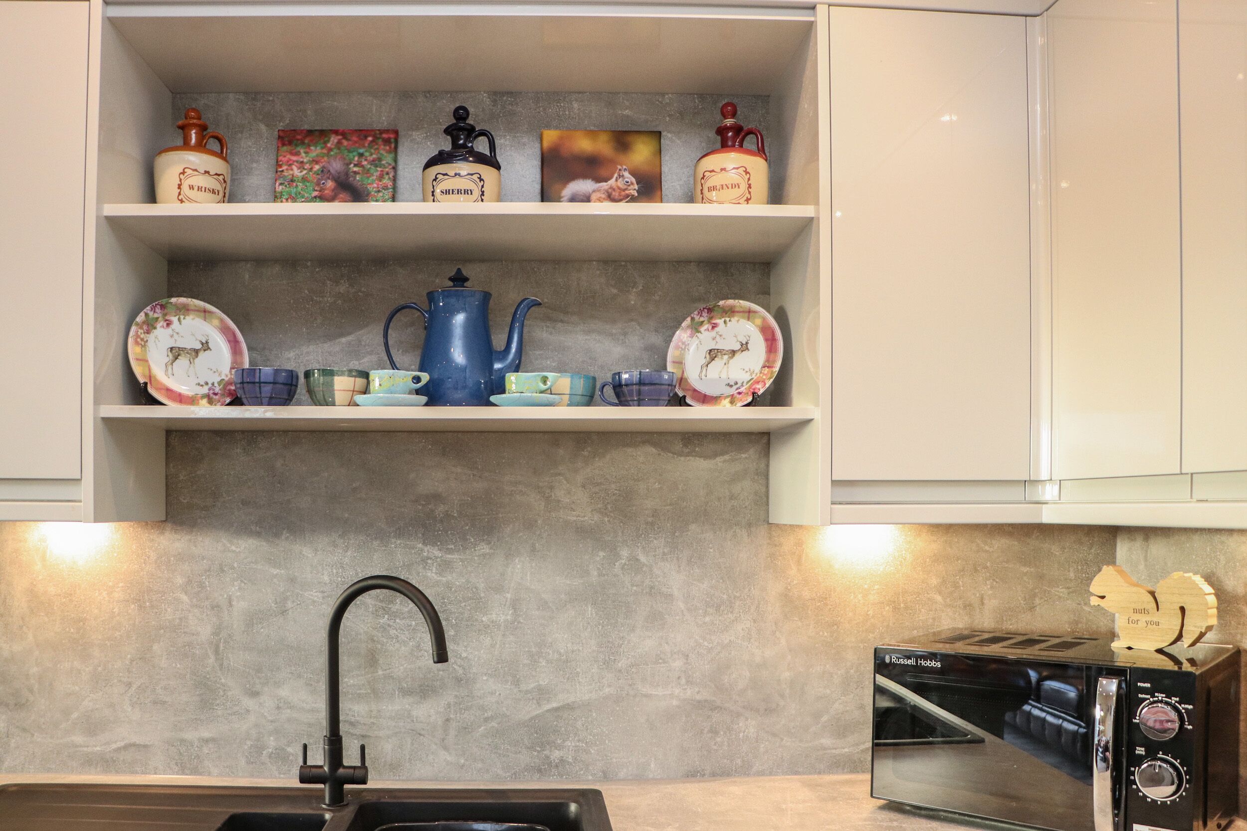 A kitchen with a modern design, featuring a sink, a toaster, and shelves with decorative items.