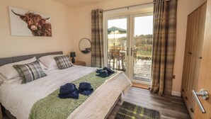 Un dormitorio con una cama, una colcha verde, una cortina a cuadros, una puerta de madera y vistas al exterior.