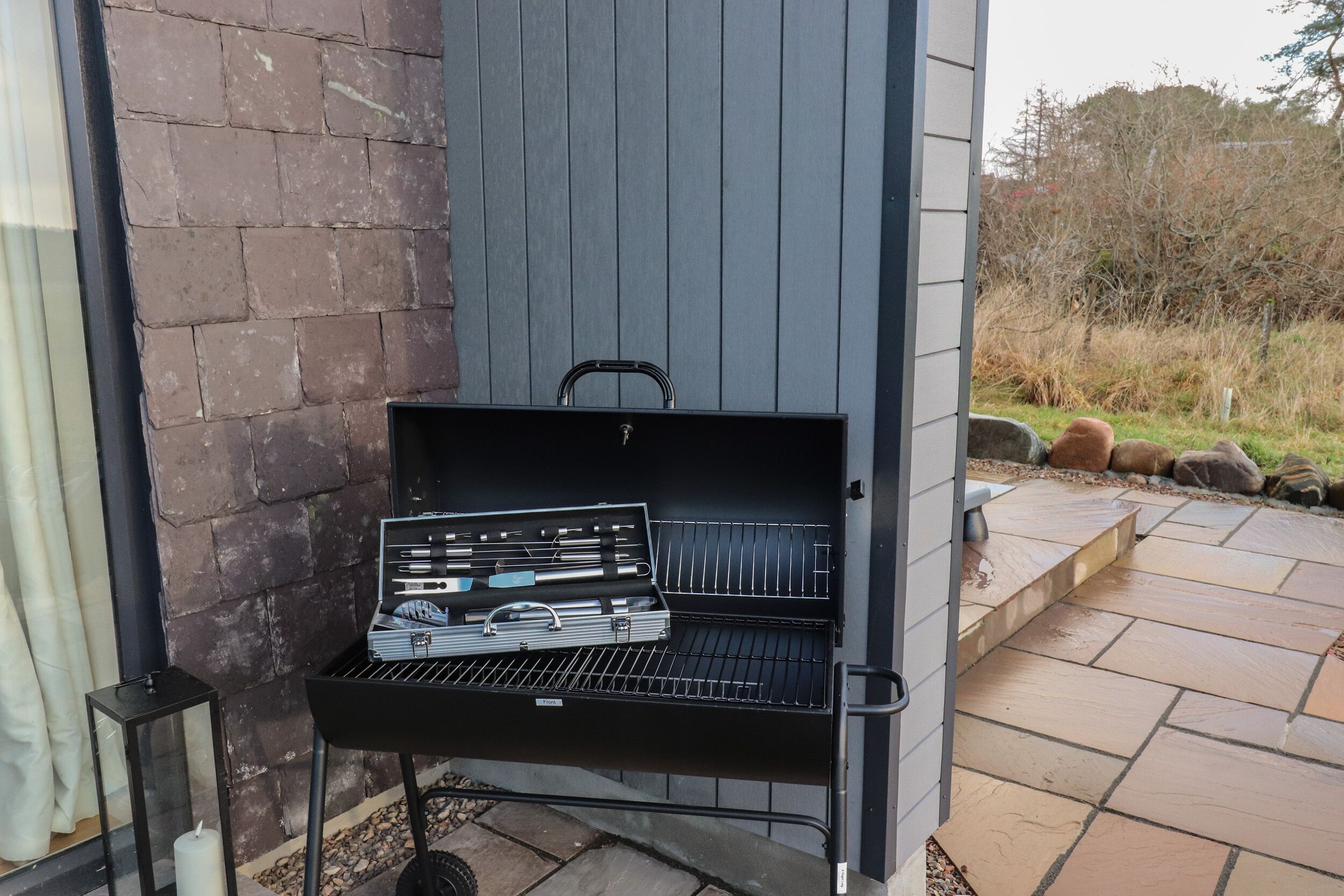 Una barbacoa portàtil amb interfaç digital, situada en un patí amb rajoles de pedra i una paret de maó.