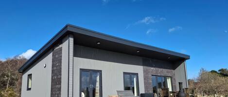 A modern two-story house with large windows, a deck, and outdoor seating.
