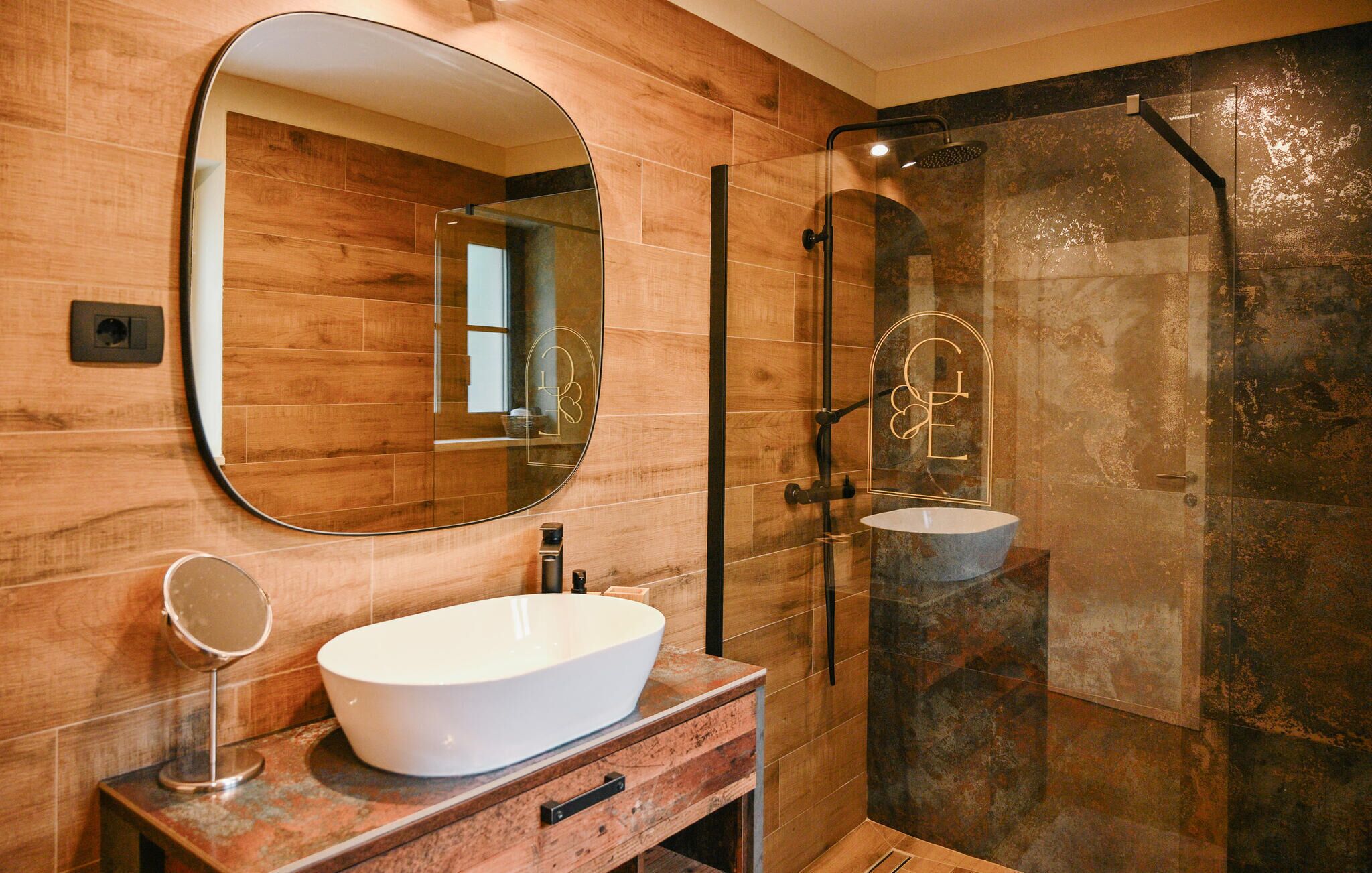 Une salle de bain moderne avec un grand miroir ovale, un lavabo blanc et une douche séparée par des parois en verre.