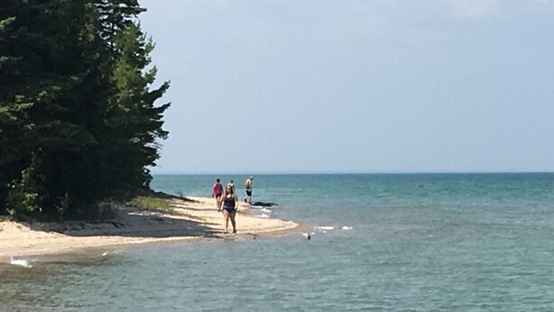 A beach with people walking along the shore, a sandy beach, and a calm sea. - Cozy rustic cabin perched above Ocqueoc Lake (Ocqueoc)