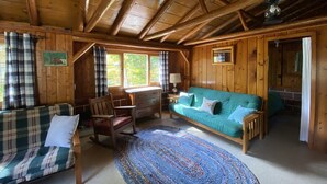 A cozy cabin interior with a wooden ceiling, a plaid sofa, a teal sofa, a rocking chair, and a patterned rug. - Cozy rustic cabin perched above Ocqueoc Lake (Ocqueoc)