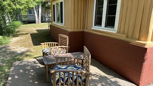 A wooden outdoor seating area with a table and chairs, a small porch, and a house with a brown and beige exterior. - Cozy rustic cabin perched above Ocqueoc Lake (Ocqueoc)