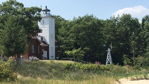 A lighthouse with a white tower and red roof, surrounded by dense green trees and a grassy area. - Cozy rustic cabin perched above Ocqueoc Lake (Ocqueoc)
