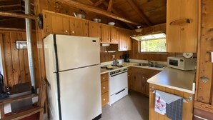 A wooden cabin kitchen with a refrigerator, stove, sink, and cabinets. - Cozy rustic cabin perched above Ocqueoc Lake (Ocqueoc)