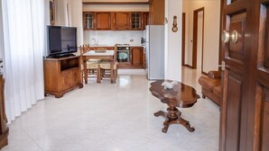 Un soggiorno con televisore, mobili in legno, un tavolo da pranzo e un angolo cottura con pensili ed elettrodomestici.