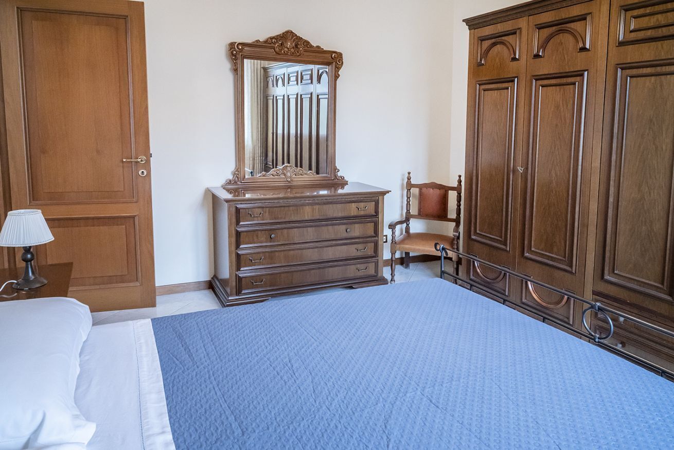 A bedroom with a bed, dresser, mirror, chair, wardrobe, and lamp.