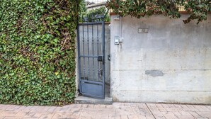 Un ingresso recintato con cancello in metallo, un muro in cemento e un vialetto in mattoni.