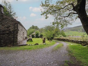 A rural setting with a stone building, a gravel path, and a grassy area with trees.