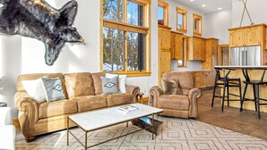 Un salon spacieux orné d’une grande tête d’ours fixée au mur, avec un canapé en cuir et un coin repas comprenant des meubles de rangement en bois et un réfrigérateur.