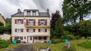 A two-story building with a balcony, a patio with outdoor furniture, and a garden area.