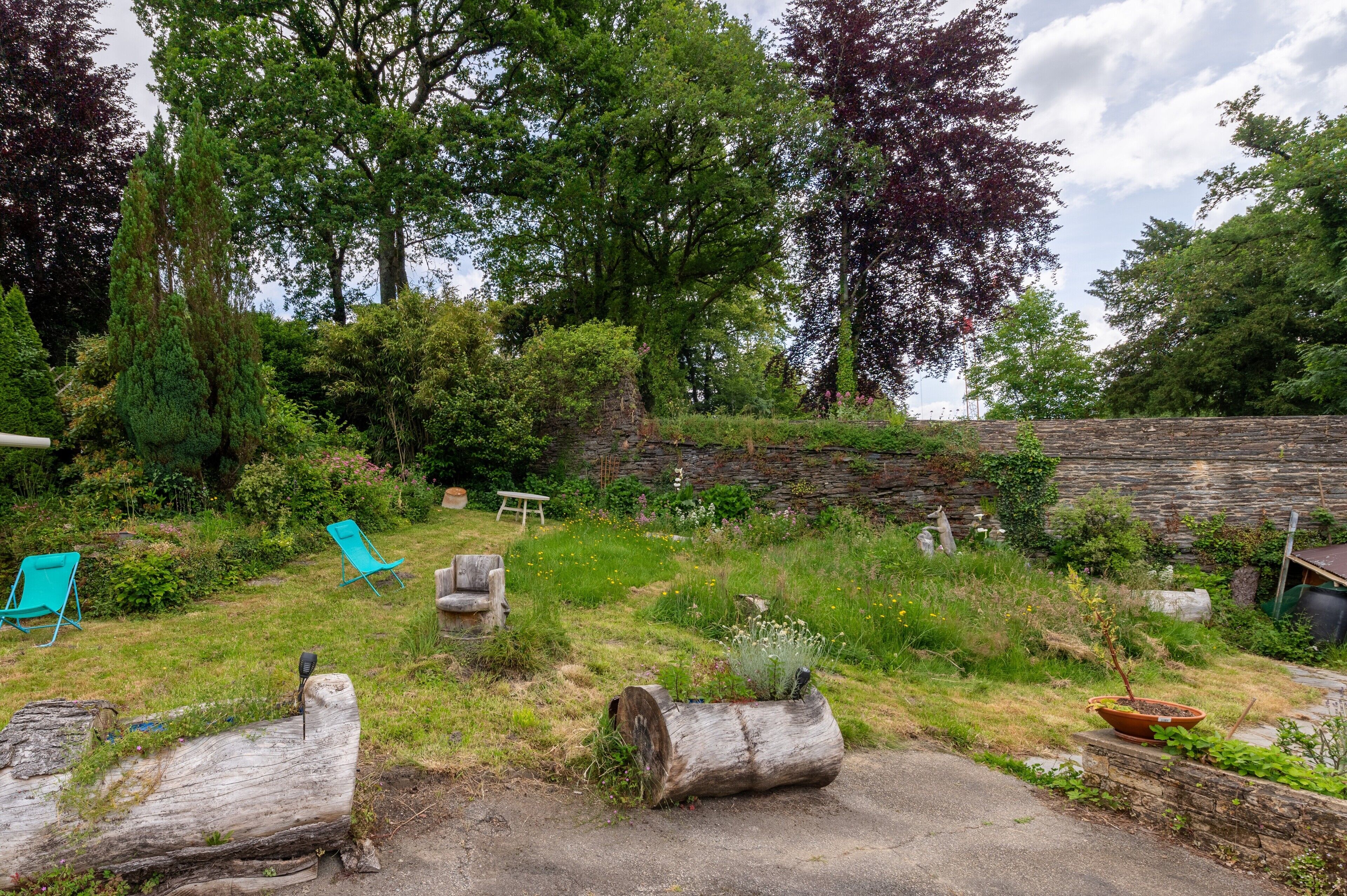 Un jardin avec un mur de pierres, une bûche et une chaise.