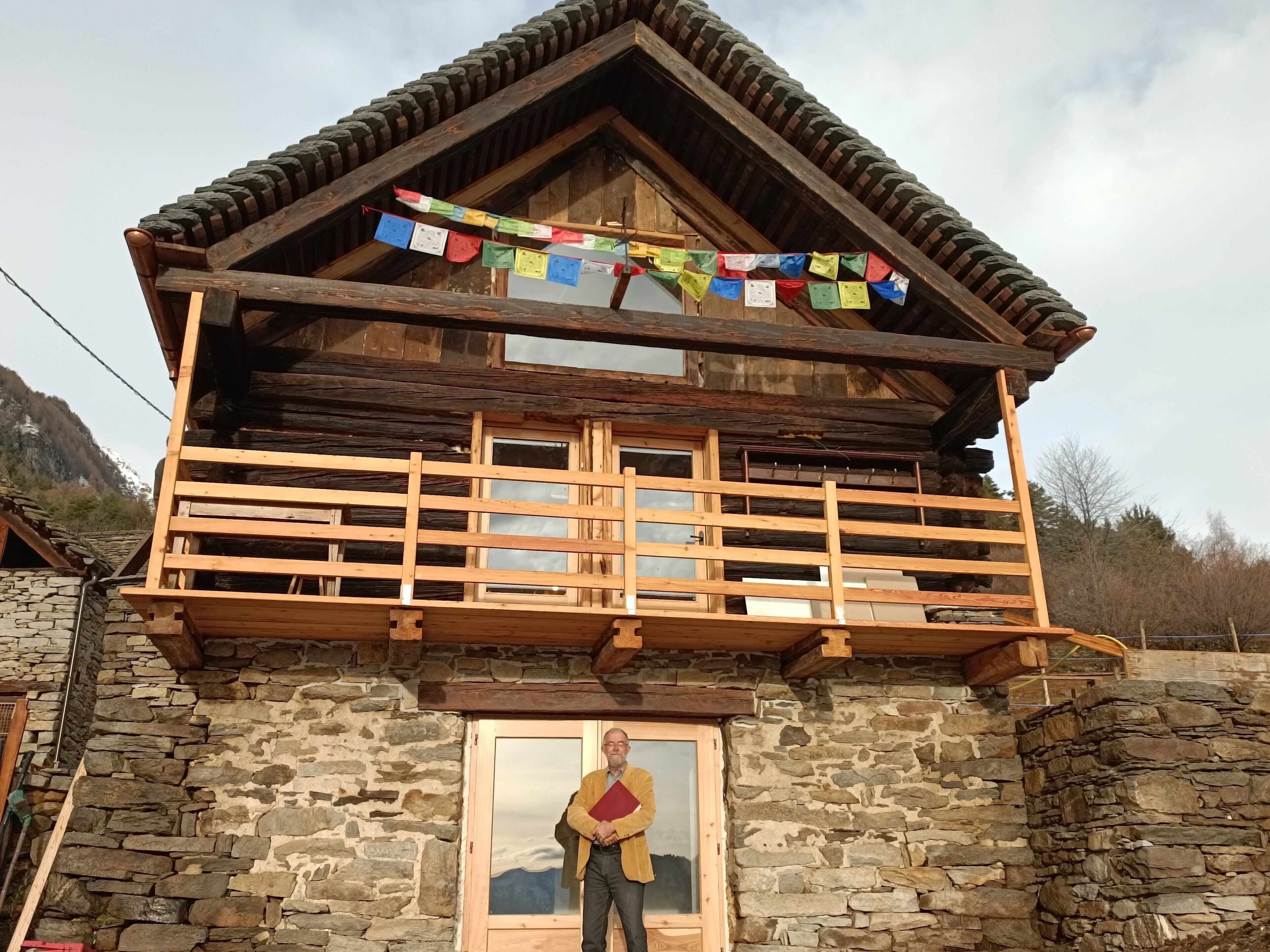 Eine Holzhütte mit Steinverkleidung, einem Balkon mit Geländern und einem Fenster mit Bergblick.