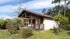 A small, single-story building with a wooden porch and a tiled roof, surrounded by trees and greenery. - Holiday Home 'Cosy Pavillon 2chambres Proche Mer' with Shared Pool, Private Terrace and Wi-Fi (Ondres)