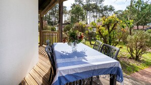An outdoor wooden deck with a table and chairs, surrounded by greenery and trees. - Holiday Home 'Cosy Pavillon 2chambres Proche Mer' with Shared Pool, Private Terrace and Wi-Fi (Ondres)