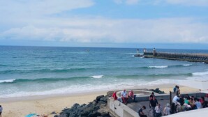 A beach with a rocky shoreline, a pier with lighthouses, and a group of people on the beach. - Holiday Home 'Cosy Pavillon 2chambres Proche Mer' with Shared Pool, Private Terrace and Wi-Fi (Ondres)