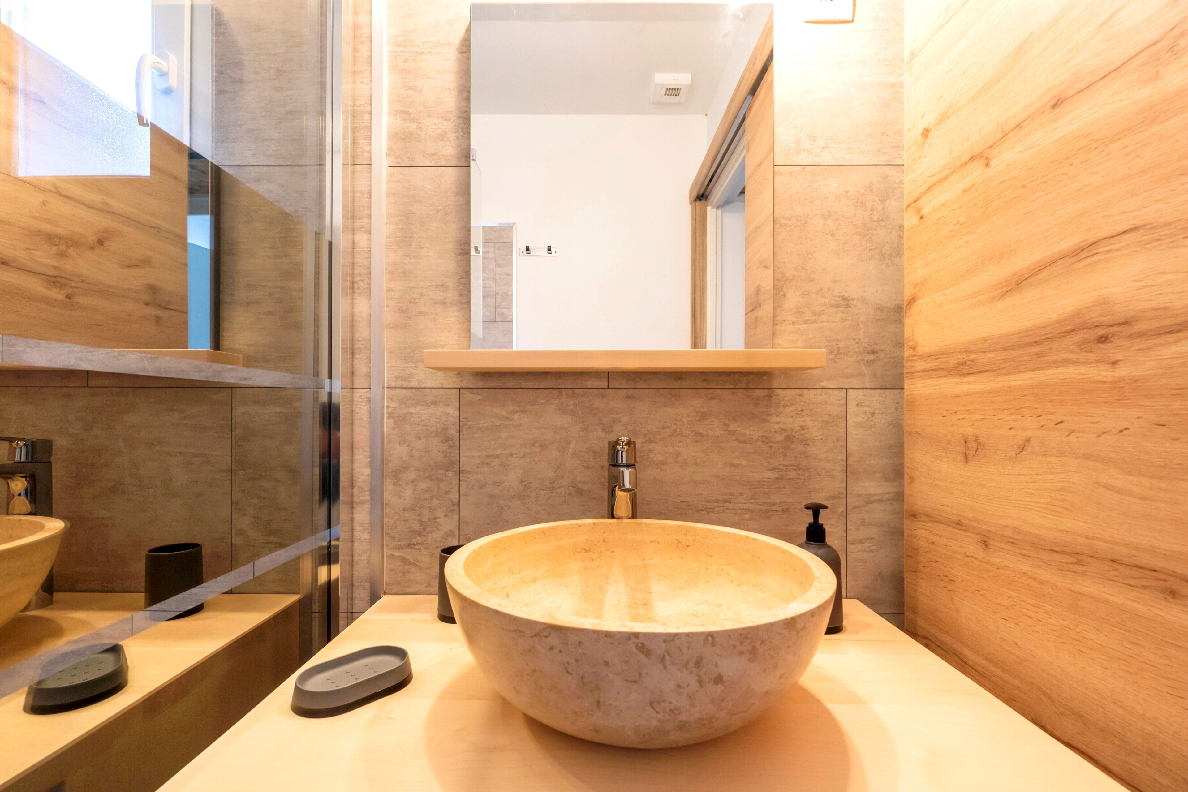 A modern bathroom with a large stone sink, a mirror above it, and a wooden vanity.
