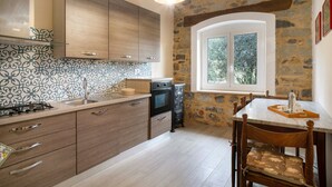 A kitchen with a stone wall, wooden cabinets, a window, and a dining table with chairs. - Apartment 'Appartamento In Villa La Baronessa' with Private Garden and Wi-Fi (Sanremo)
