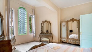 A bedroom with a bed, two dressers, a vanity with a mirror, and a window with a green frame. - Apartment 'Appartamento In Villa La Baronessa' with Private Garden and Wi-Fi (Sanremo)