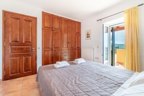 Quarto com cama, armário de madeira e vista através de uma porta de vidro.