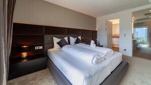 Ein modernes Schlafzimmer mit einem großen Bett, einem Kopfteil mit eingebauten Regalen, Nachttischen und Blick auf den Balkon.