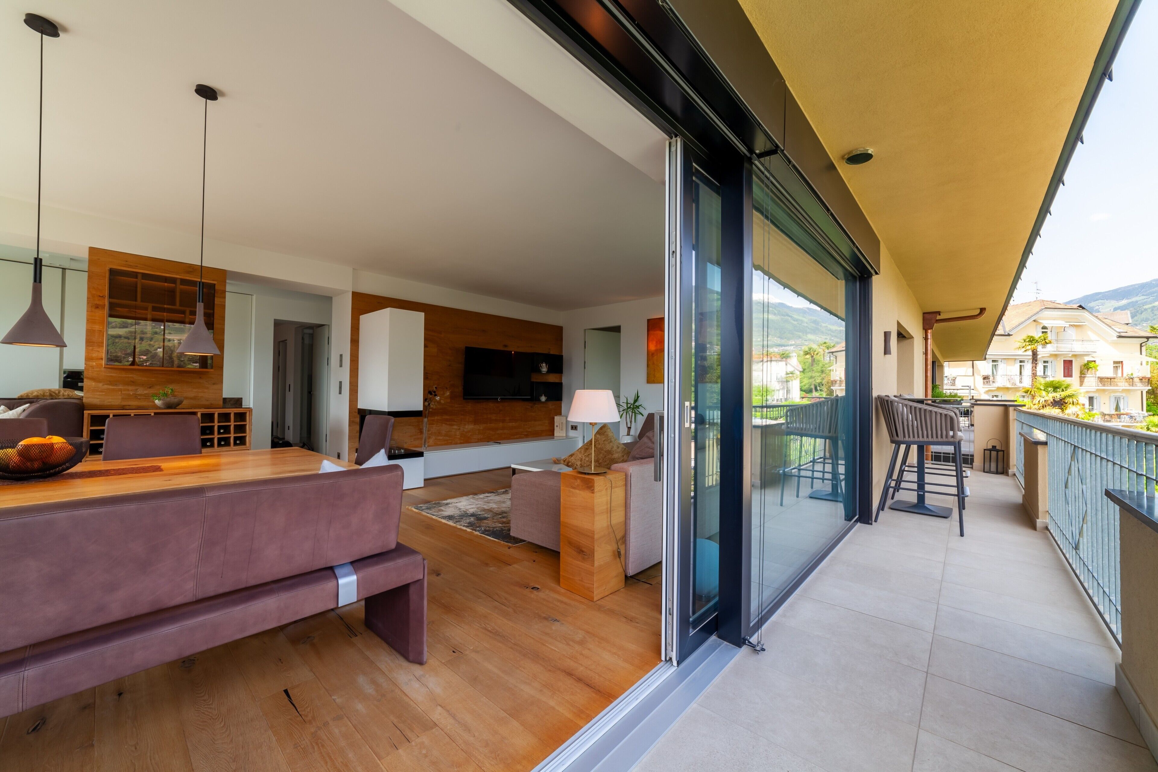 Un salon moderne avec un plancher en bois, un canapé, une table  à manger et un balcon offrant une vue sur les environs.