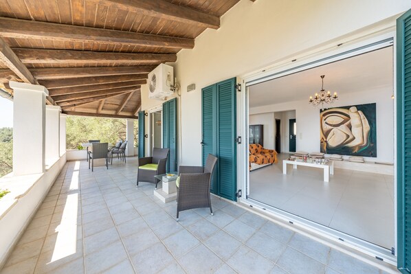 Un patio techado al aire libre con mobiliario de mimbre, una mesa de comedor y vistas al interior.