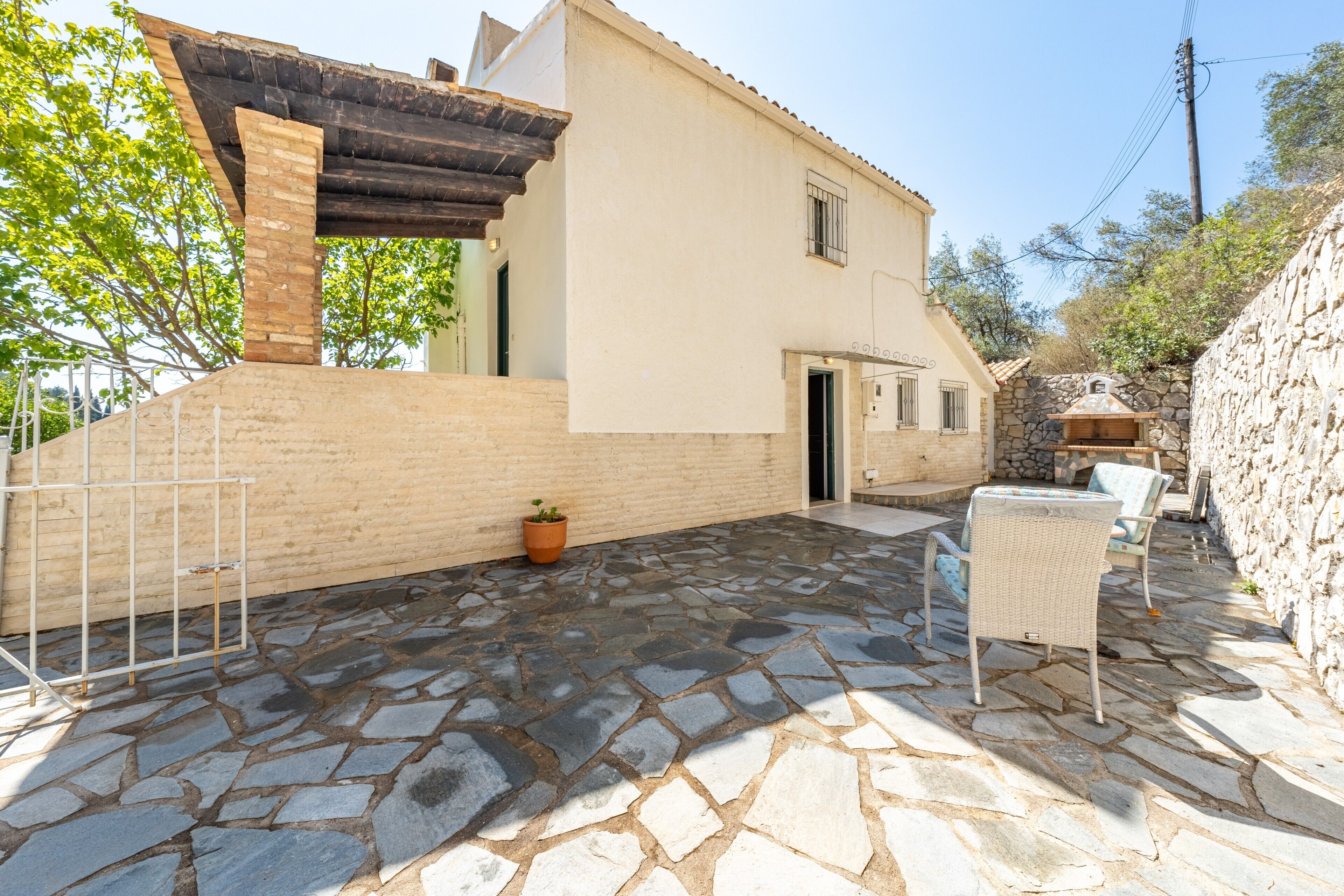 Un patio empedrado con mobiliario exterior, un muro de ladrillo y un edificio con tejado de baldosas.