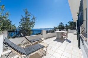 A terrace with sun loungers and a table, overlooking a body of water and hills. - Studio Apartment 'Salvia' with Sea View, Wi-Fi and Air Conditioning (Corfu)