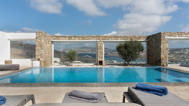 Una piscina infinita con agua azul cristalina, paredes de piedra y sillones de descanso con toallas.