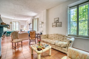 Un salon comprenant un canapé, des fauteuils, une table basse et une fenêtre donnant sur un paysage verdoyant.