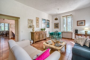 Un vaste espace de vie comprenant un canapé, une table basse et une table à manger avec des chaises. Les murs sont ornés de tableaux encadrés et une fenêtre offre une vue agréable.