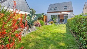 Una casa moderna con un jardín bien cuidado, un patio con mobiliario exterior y un cielo despejado.