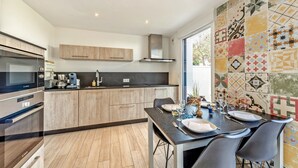 Una cocina moderna con horno Bosch, una mesa de comedor preparada para cuatro personas y un colorido salpicadero de azulejos.