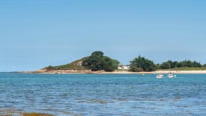 Paisaje costero con una colina, playa y barcos.