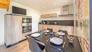 Una cocina moderna con una mesa de comedor para cuatro personas, equipada con horno empotrado y microondas, y un televisor de pantalla plana grande montado sobre la encimera.