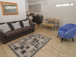 A modern living room with a brown sofa, patterned cushions, a blue armchair, a dining table with chairs, and a kitchen in the background.