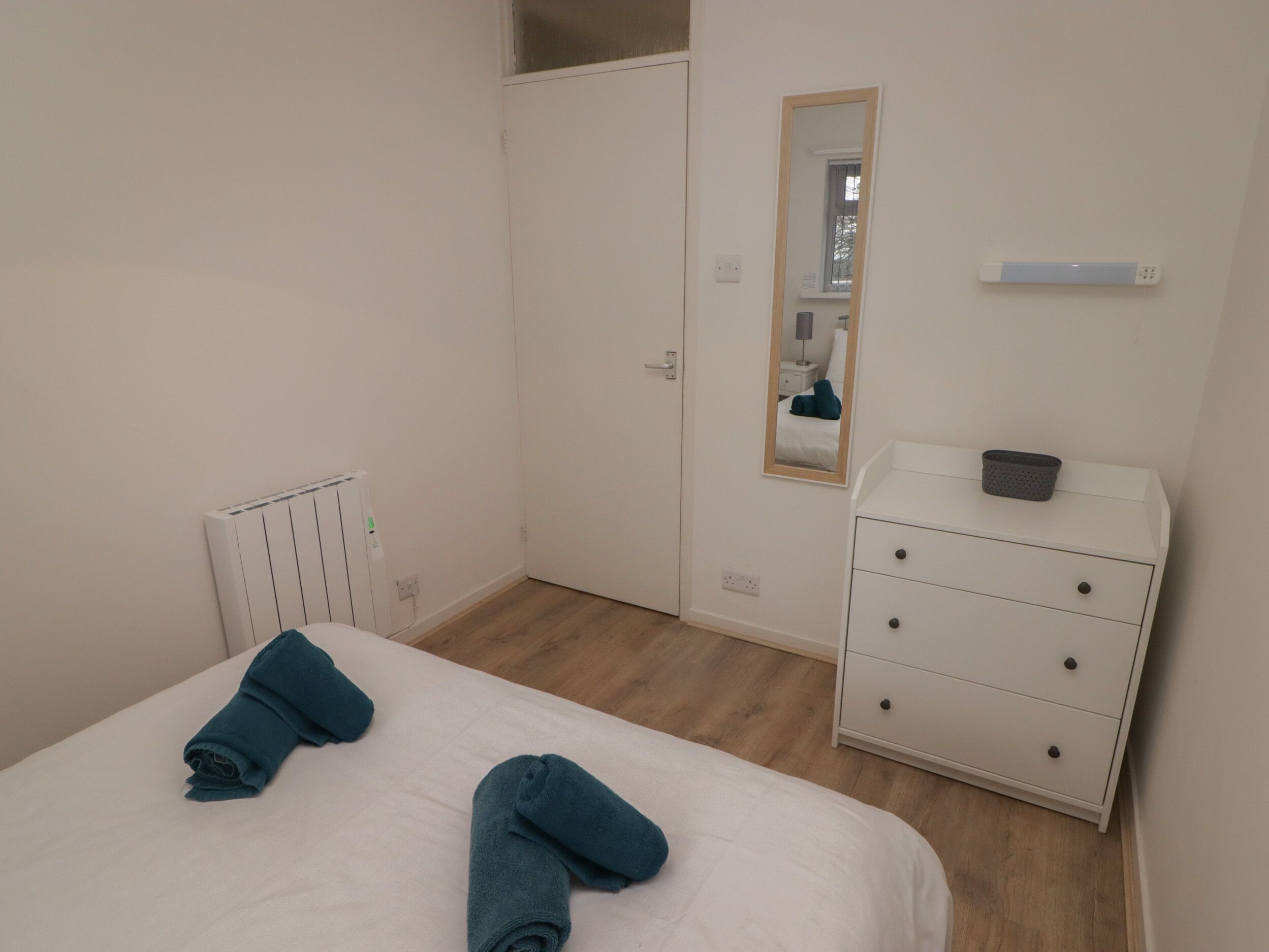 A bedroom with a bed, a dresser, a mirror, and a radiator.
