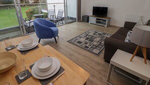 A modern living room with a dining area, a sofa, a TV, and a view of the outdoors. - 19 Coedrath Park (Saundersfoot)